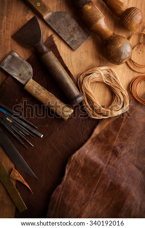 Leather craftmans work desk . Piece of hide, thread and working tools on a work table. Intentionally shot in low key.