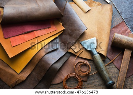 Leather craft or leather working. Selected pieces of beautifully colored or tanned leather on leather craftman\'s work desk . Piece of hide and working tools on a work table.