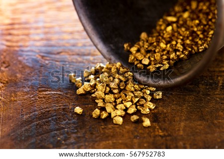 Profit, trade and exchange. Gold nuggets spilling out from a grungy old metal container, placed on a old wooden table.Shallow depth of field.
