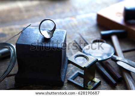 Jewelry making. Silver jewelry or ring on a old anvil, with tools in background. intentionally shot in nostalgic tone. Shallow depth of field.