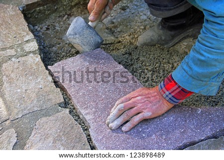 senior landscape gardener fitting a flagstone tile with a rubber mallet
