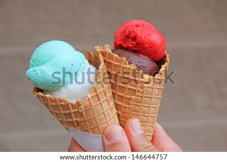 mans hand holding two ice cream wafers with various scoops