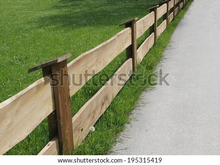 wooden fence made of planks and green meadow, diagonally, country road