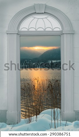view through arched door, sunset at wintry lake in the alps