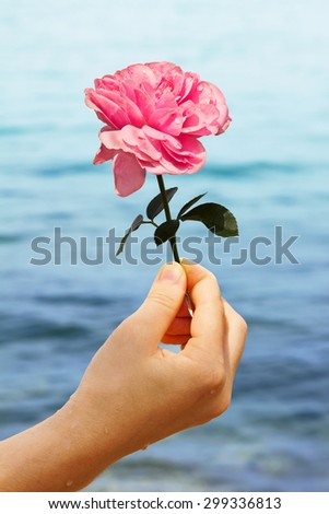 girls hand holding a pink rose, lake background with waves