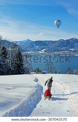 father and son at a tobogganing route in the bavarian alps, view to lake tegernsee, hot air balloons