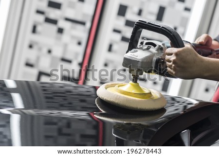 Car polishing series : Closeup of worker\'s hand using tool to buffing black car hood in garage with copy space on the left