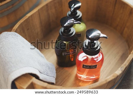 Colorful bath gel, shampoo, lotion bottles and grey towel in wooden bucket with vintage effect