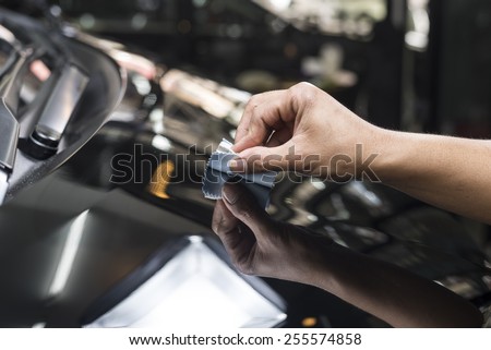 Car polishing series : Closeup of worker\'s hand using small sponge cover with tiny light blue cloth waxing black car hood in garage