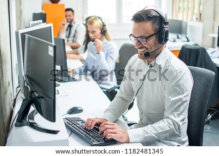 Young male technical support dispatcher with headset talking with customer in call center