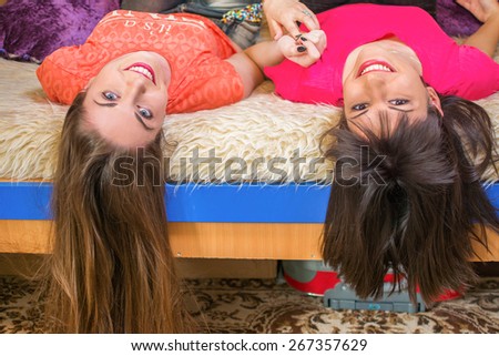 Teen girls lying on couch upside down, looking at camera, smiling.