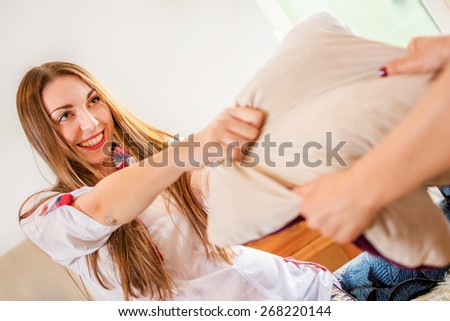 Young woman having pillow fight in bedroom.