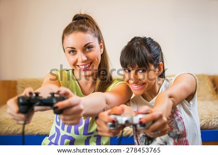 Two girls play video games on the joysticks at home.