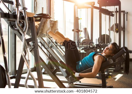 Side view of a fit young woman doing leg presses in the gym.
