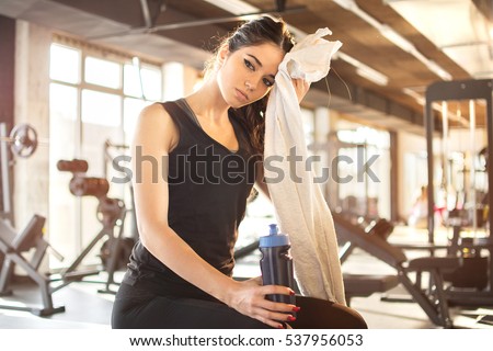 Tired girl wiping sweat with towel in gym.