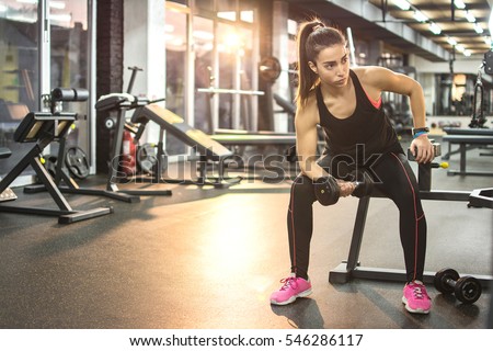 Young sportswoman lifting weights in gym.
