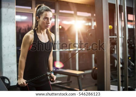 Young sporty girl working out on pull-down machine in gym.