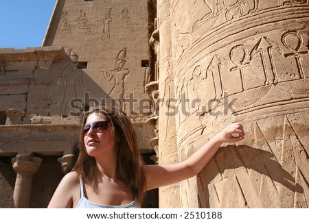 Young Woman soaks up the Sun leaning against a Temple Pillar with hieroglyphs depicting The Key Of Life, and Fertility at The Temple of Horas on The Nile, Egypt