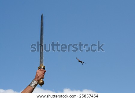 Roman Sword with golden Bird of Pray at the hilt is thrust skywards in victory with Bird of Pray swooping