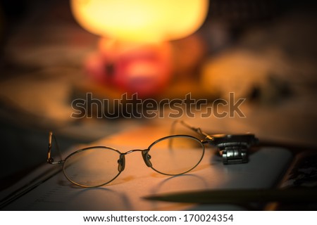 Vintage still life with old spectacles on book near desk lamp