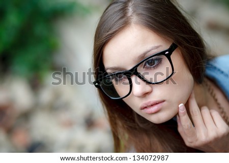 young female wear glasses holding rim with fingers looking sideways closeup