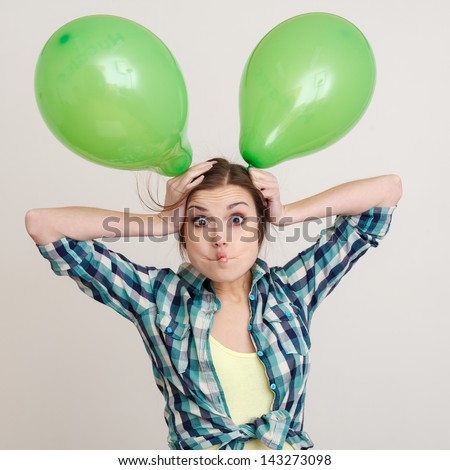 young woman playing with two green balloons making face studio shot