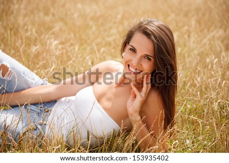 gorgeous young woman lying down on grass touching her face with fingers smiling looking at camera