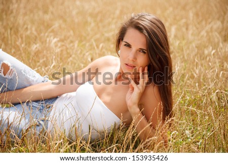 gorgeous young woman lying down on grass touching her face with fingers posing looking at camera