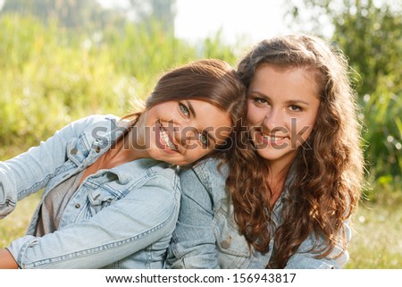 two girlfriends in jeans wear outdoors sitting  smiling looking at camera