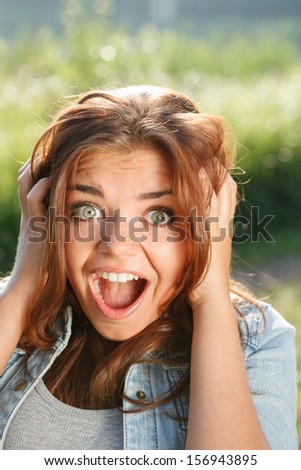 close-up portrait of shocked with good news teenage girl outdoors with mouth opened looking at camera