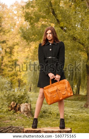 full length portrait of young female standing on stump in forest with bag looking away