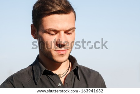 close-up portrait of sad young man looking down clean blue sky on background