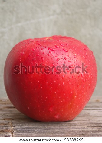 Big red apple with water drops on wooden table.