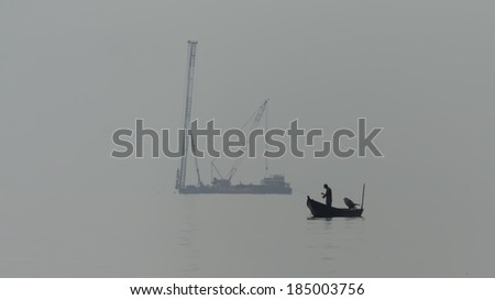 Silhouette fisherman catching fish in fog with piling ship background