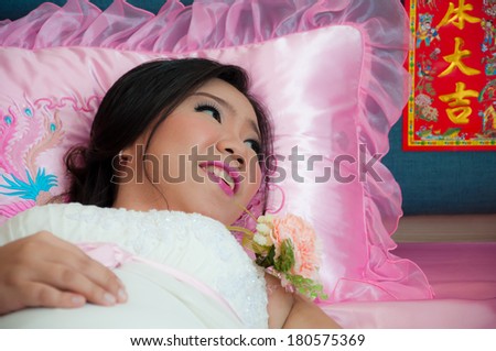 Bride lays on the bed looking at her groom after marriage ceremony as Chinese Traditional