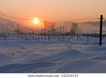The village is covered with snow, lit the rising sun.
