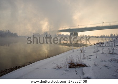 Bridge over the river with snowy banks covered with mist