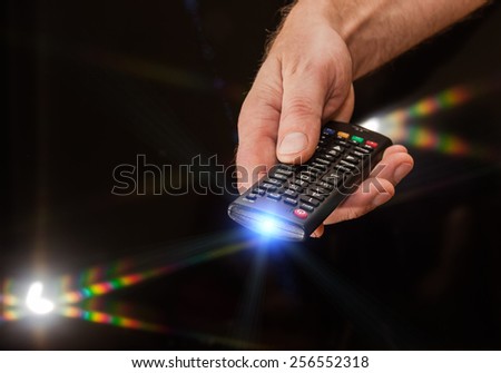 TV remote control in man\'s hand on a dark background with flare light