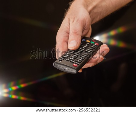TV remote control in man\'s hand on a dark background with flare light