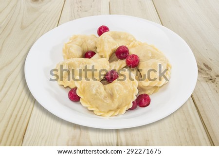 Ukrainian varenyky (dumplings) filled with sour cherry and cherries in powdered sugar on white dish on a wooden surface