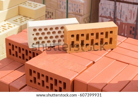 White brick with a round holes and yellow brick with a rectangular holes from above on a pallet with the red perforated bricks on the background of other bricks on a warehouse