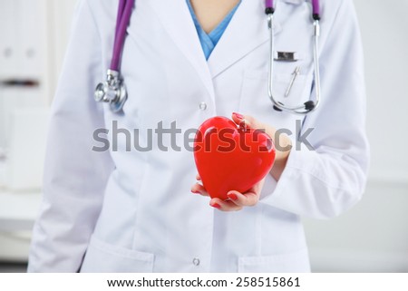 Young female doctor with stethoscope holding heart over white background.