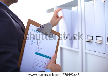 Man's hand holding big folder from the shelves with office files