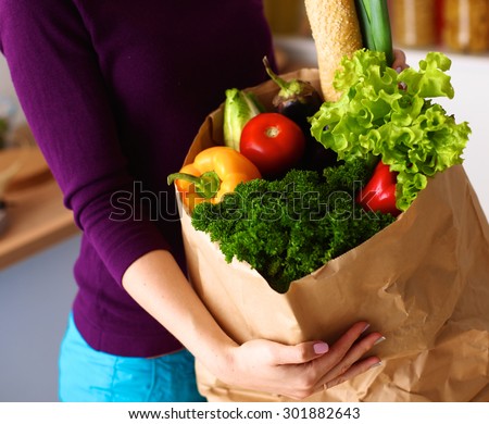 Assorted fruits and vegetables in brown grocery bag holding a young girl