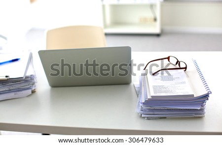 a stack of papers on the desk with a computer