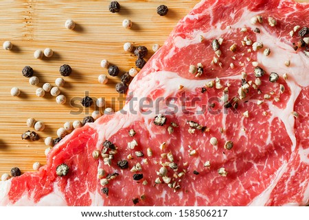 Close up aged beef ribeye steak with black and white pepper on bamboo chopping board