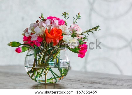 Close up rose and carnation flower bouquet in glass vase on wooden table