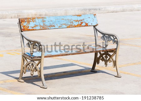 Old and weathered wooden bench with cast aluminium legs on concrete floor in strong sunlight