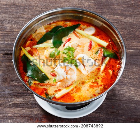 Tom yam koong - Thai spicy prawn or shrimp and lemon grass soup with mushrooms in stainless steel hot pot on old wooden table
