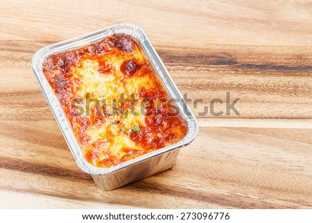 Close up beef lasagna in foil tray on wooden chopping board, deep focus image, delicatessen